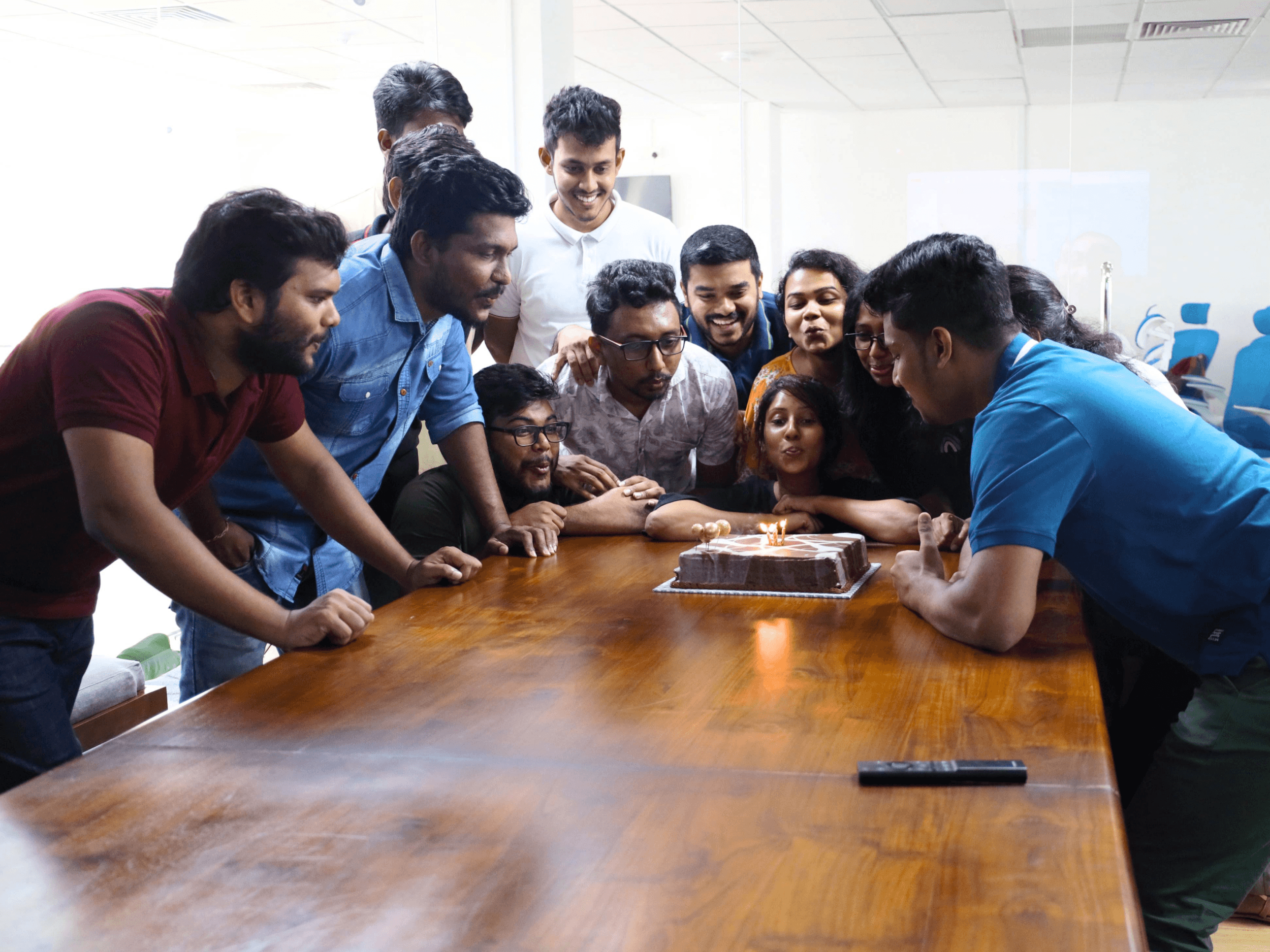 Office team celebrating a milestone by blowing out candles on a cake