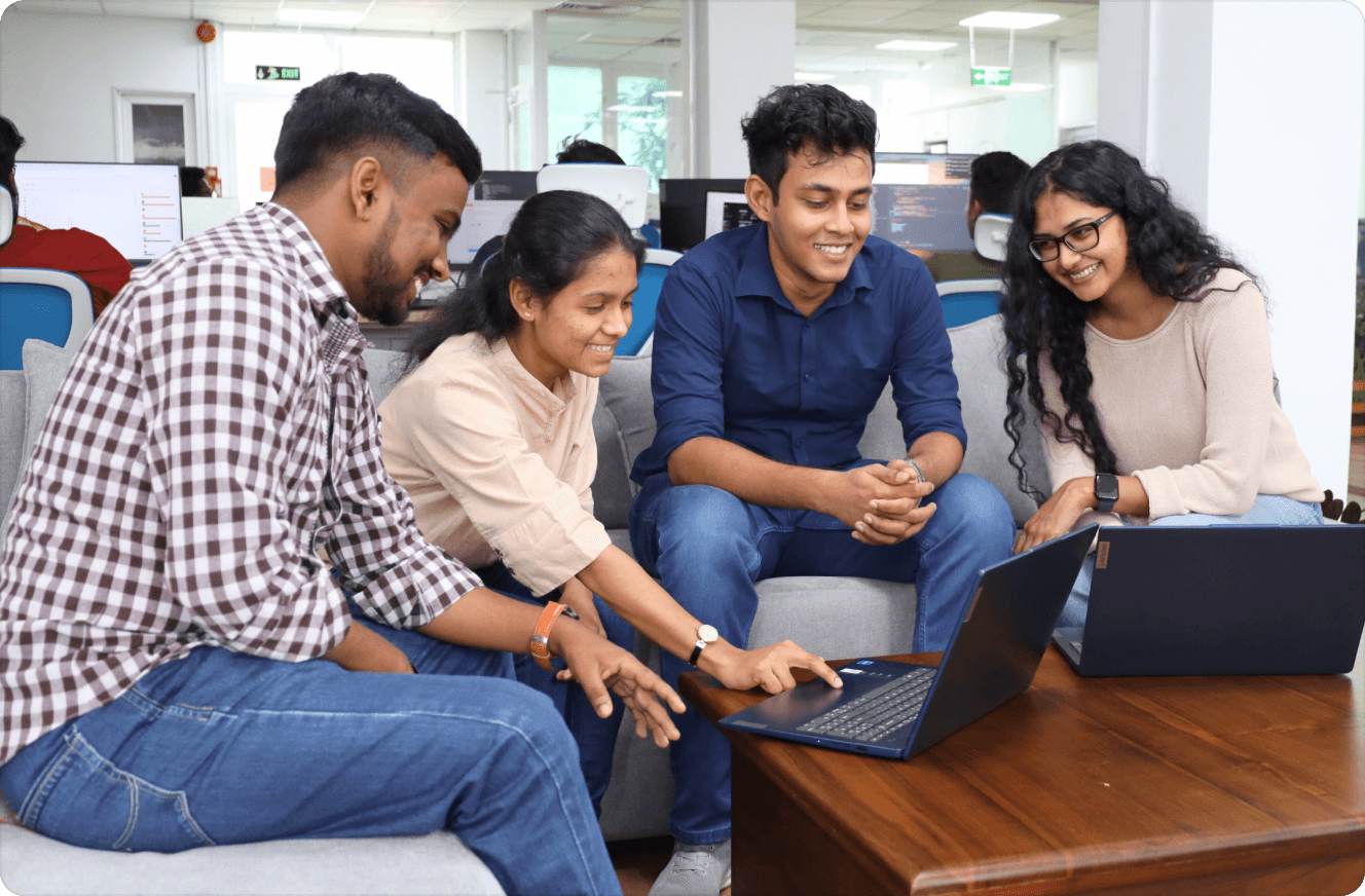 Team members smiling and collaborating on a laptop while relaxing on a couch